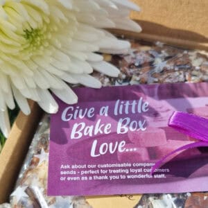An open BakeBox Gift showing wrapped pieces of chocolate brownie with a card that says "Give a little BakeBox Love" and a white flower.