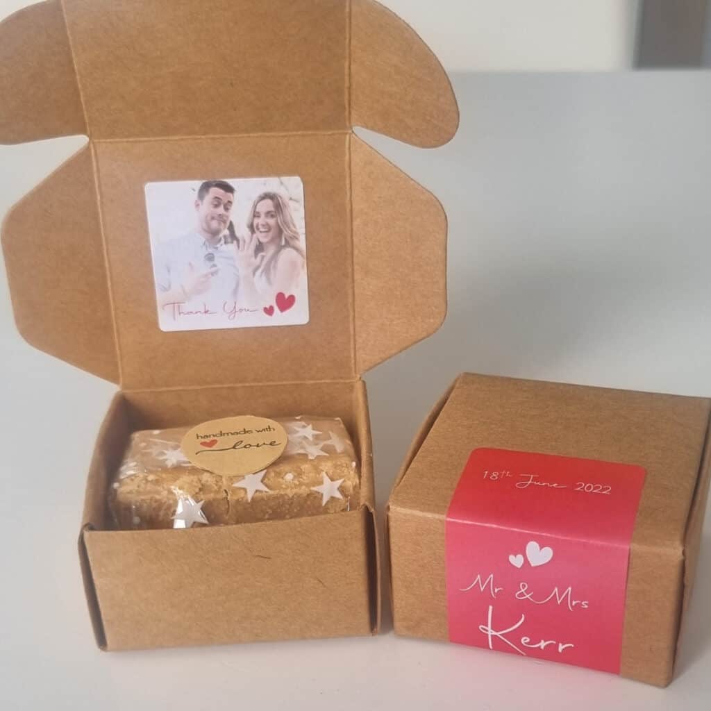 An open wedding favour box of Scottish Tablet with a picture of a couple next to a closed box with their names and wedding date.